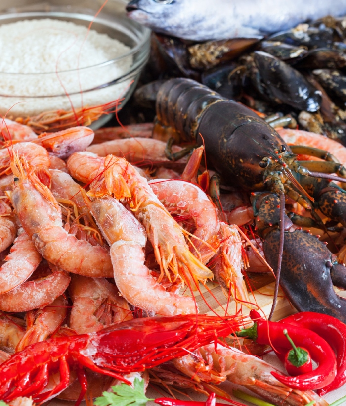 Assortiment de fruits de mer frais avec crevettes, homard, moules, poisson et piments rouges sur une table de préparation.